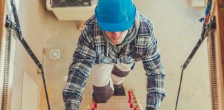 Construction Worker Walking Upstairs To Take a Look at House Attic. Wooden Second Level Stairs.