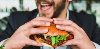 person holding burger bun with vegetables and meat