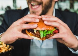 person holding burger bun with vegetables and meat