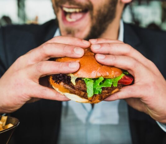person holding burger bun with vegetables and meat