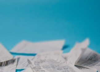 Selective focus of stack of white paper wrinkled receipts in daylight on blue background