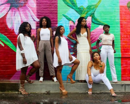 six women wearing white pants posing