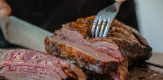 person slicing a meat on brown wooden board