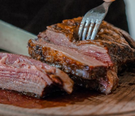 person slicing a meat on brown wooden board