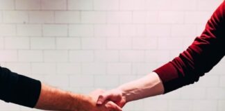 two person shaking hands near white painted wall