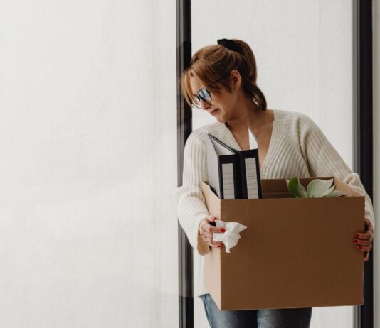 a woman crying while carrying her items in a box after being a victim of a debt relief scam.