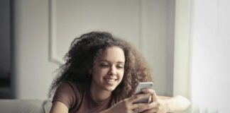 Photo of Smiling Woman Sitting on a Gray Bean Bag While Using Her Phone