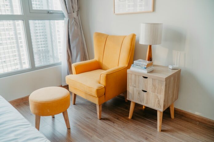 Photo by Di_An_h yellow armchair and stool beside wooden nightstand by the wall near glass window and bed