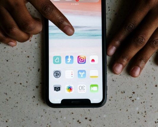 Close-up view of hands interacting with social media apps on a smartphone screen.