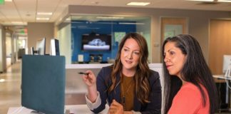 two women sitting at a table looking at a computer screen