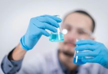 5 Common Data Management Mistakes in Clinical Trials (And How EDC Solves Them) Scientist in a laboratory conducting an experiment, holding blue liquid in flasks with protective gloves.
