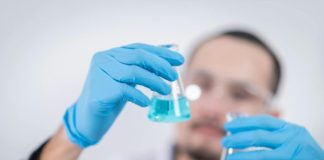 Scientist in a laboratory conducting an experiment, holding blue liquid in flasks with protective gloves.