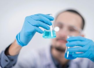 5 Common Data Management Mistakes in Clinical Trials (And How EDC Solves Them) Scientist in a laboratory conducting an experiment, holding blue liquid in flasks with protective gloves.