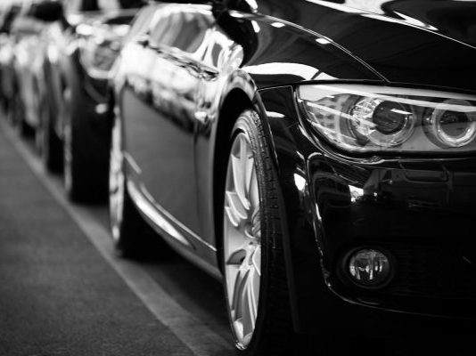 Close-up black and white image of a luxury car line-up focusing on vehicle headlights.