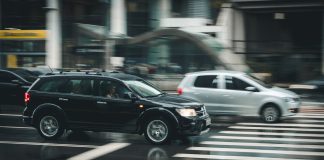 Vehicles speeding through a city street with a visible zebra crossing and blurred motion effect.