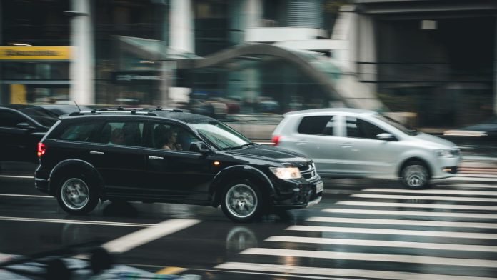 Photo by Kaique Rocha Vehicles speeding through a city street with a visible zebra crossing and blurred motion effect.