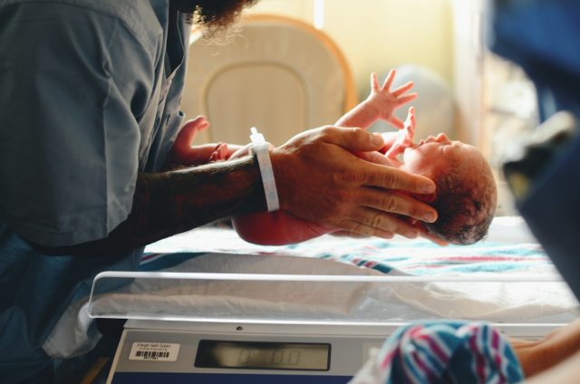 Photo by Christian Bowen person wearing gray shirt putting baby on scale