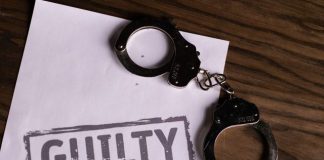 Top view of handcuffs on paper with 'GUILTY' text, symbolizing a verdict or crime.