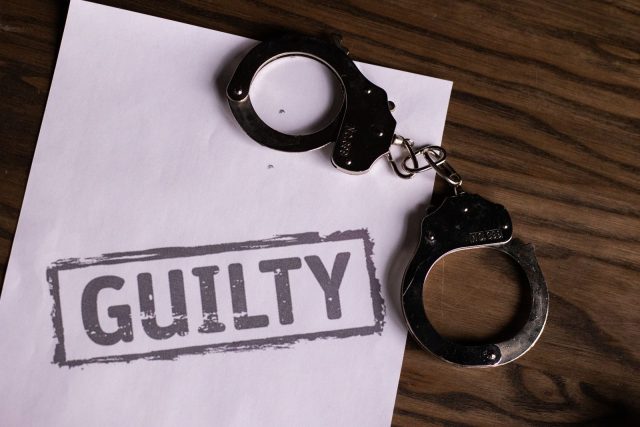 Photo by KATRIN BOLOVTSOVA Top view of handcuffs on paper with 'GUILTY' text, symbolizing a verdict or crime.